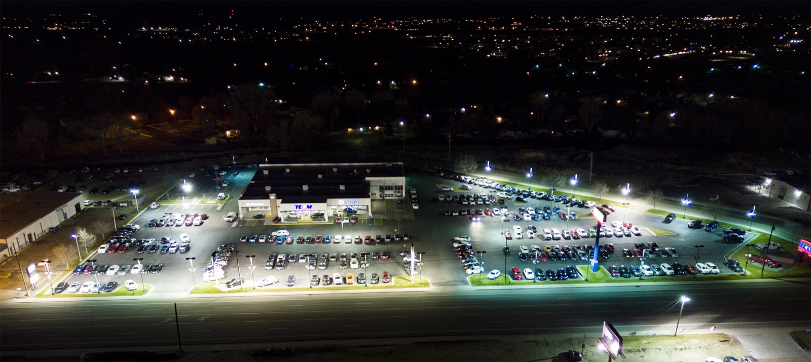 Dealership lot at night before upgrade — scattered pools of light and dark rows