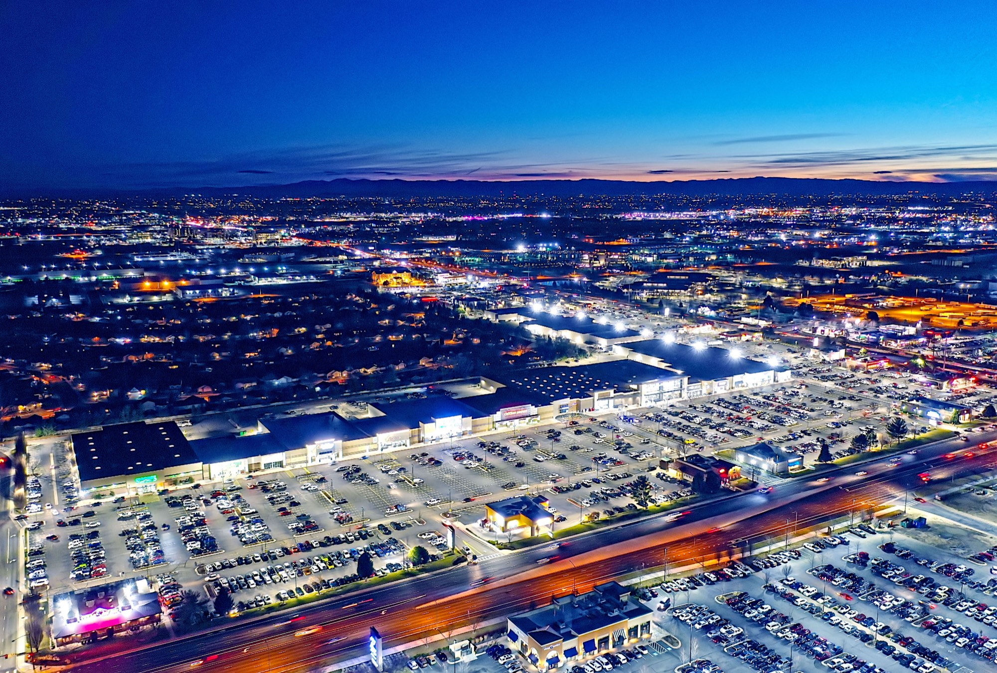 Dusk aerial of Meridian Crossroads — R9 parking lot lighting, bright and uniform across the full retail center