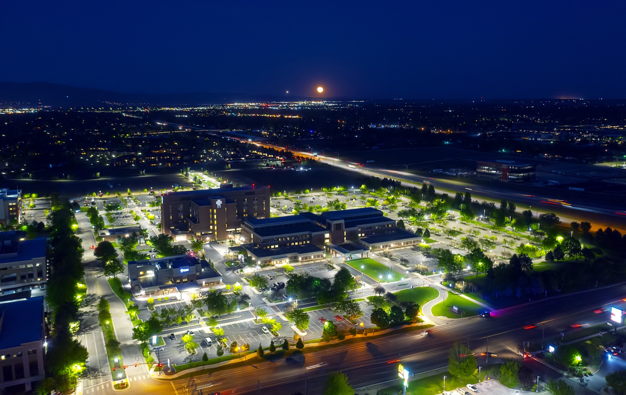 Aerial of St. Luke's Meridian hospital campus at night under a rising moon — R9 parking lot lighting across the entire medical campus