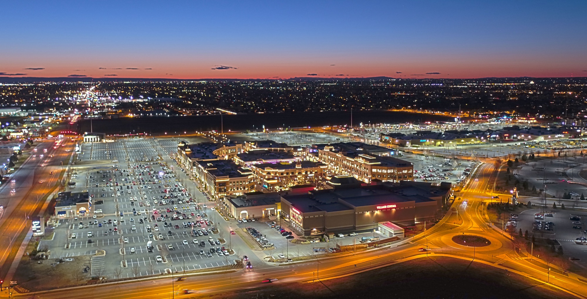Dusk aerial of The Village — R9 parking lot lighting glowing evenly across the entire property