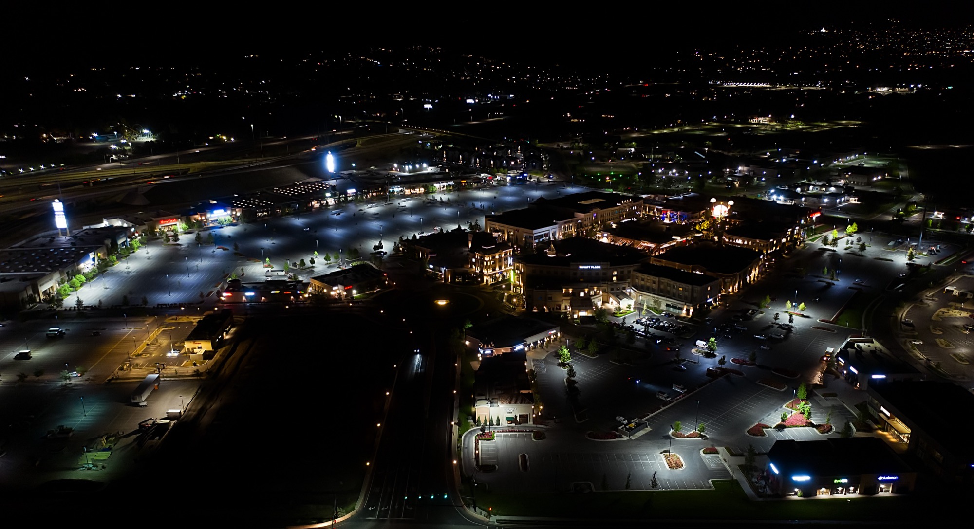Aerial of a retail site at night before R9 — harsh bright pools directly under some poles, large dark voids between them